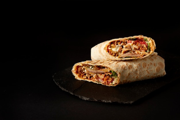 Shawarma, roll in lavash , grilled meat, with vegetables, sandwich , cut on a black table, horizontal, copy spase