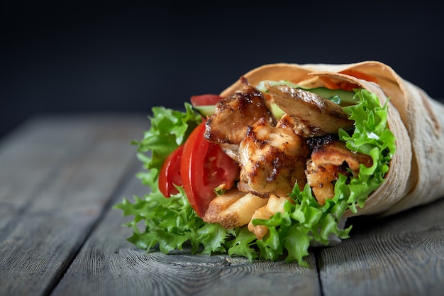 Shawarma rolled in lavash with grilled meat and vegetables on wooden background