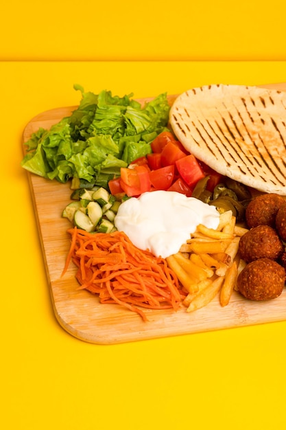 Shawarma with falafel on a wooden board side view on a yellow background