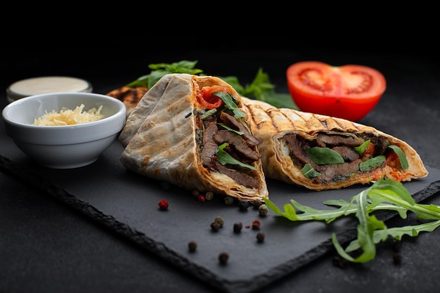 Shawarma with meat cheese tomatoes and sauce on a black background