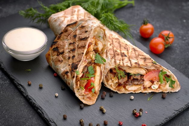 Shawarma with meat, cutaway, with sauce, tomatoes, cheese, herbs and garlic, on black slate, on a black background