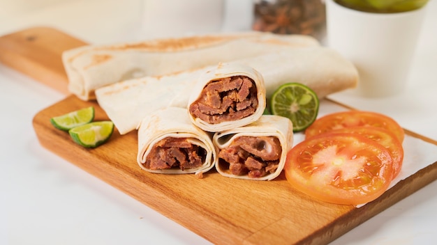 Shawarma with meat, mayonnaise, tomato and lime on a wooden cutting board