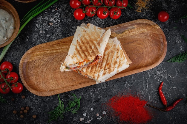 Shawarma with vegetables on a wooden board with pita sauce on a dark stone table decorated with cherry tomatoes Fast food restaurant delivery service