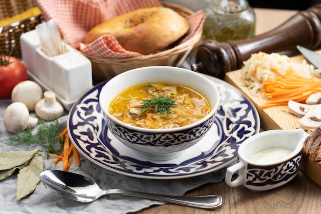 Shchi with sour cream - a traditional Russian vegetable soup made of cabbage, potatoes, carrots and mushrooms in a plate with a traditional Uzbek 