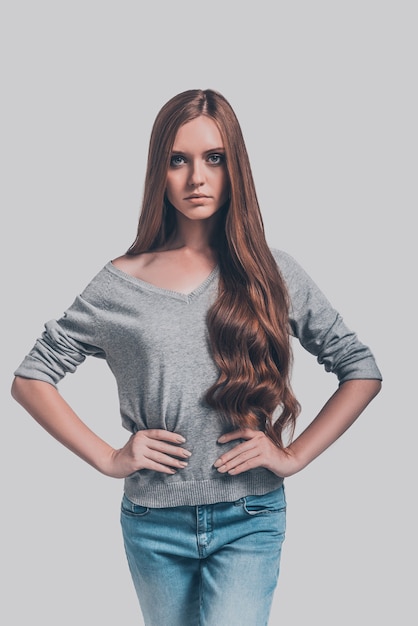 She is beautiful. Studio shot of attractive young woman in casual wear holding hands behind back and looking at camera