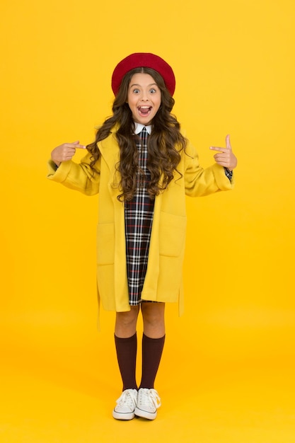 She is so surprised little girl in coat going to school education concept school and fashion child in pupil uniform kid in french beret on yellow background stylish teen college student