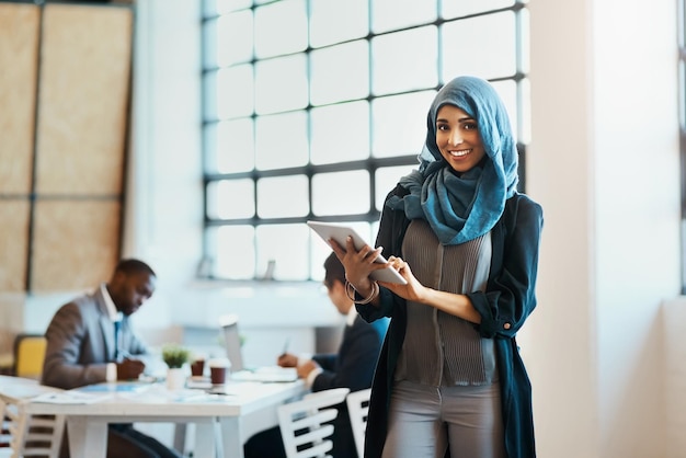 She keeps track of the work progress in the company Portrait of a confident young businesswoman browsing on a digital tablet while standing in the office at work