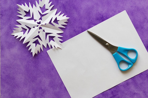 Sheet of paper scissors to make snowflake on the violet surface