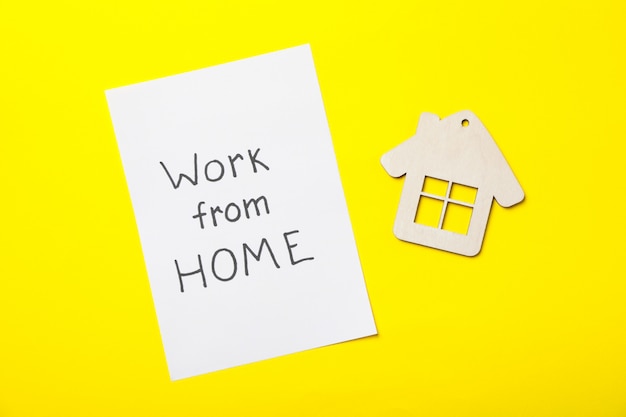 Sheet with inscription Work from home and house on yellow surface