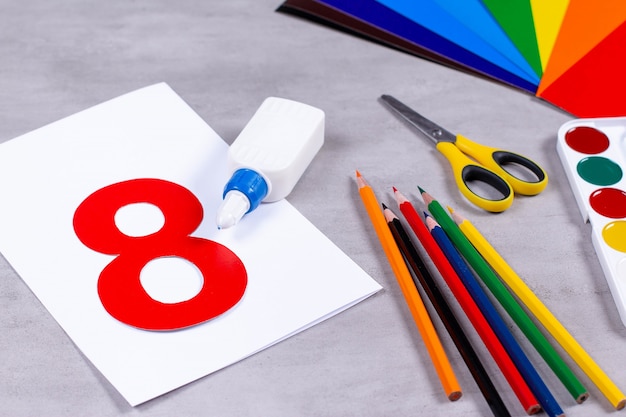 Sheets of paper, glue and scissors on a table. March 8 from paper. Children's art project, a craft for children. Craft for kids.