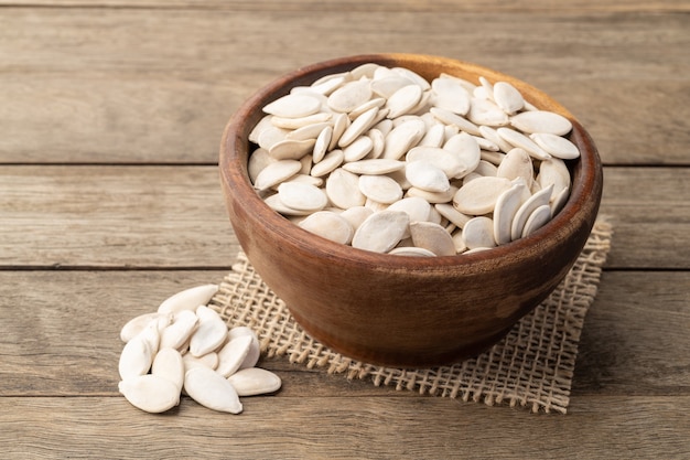 Shelled pumpkin seeds in a bowl over wooden table.