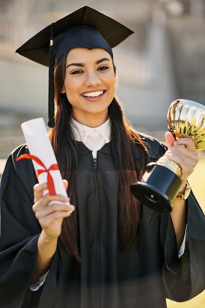 Shes achieved outstanding merit Portrait of a student holding her diploma and trophy on graduation day