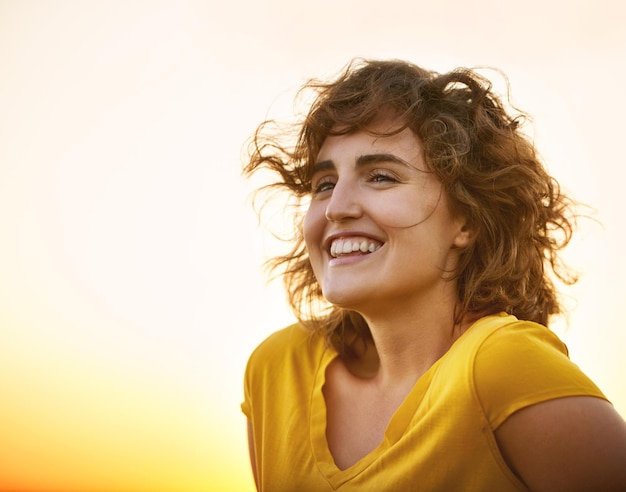 Shes got sunshine in her soul Shot of a cheerful young woman smiling while standing outside at sunset