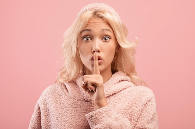 Photo shh keep silence young woman showing secrecy gesture gesturing hush on pink studio background