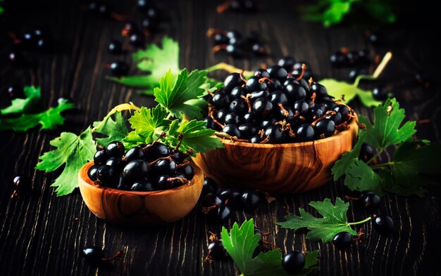 Shining fresh black currants in wooden bowls summer harvesting black kitchen table background place for text selective focus