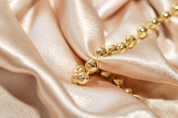 Shiny golden textured silk background in folds with beads.