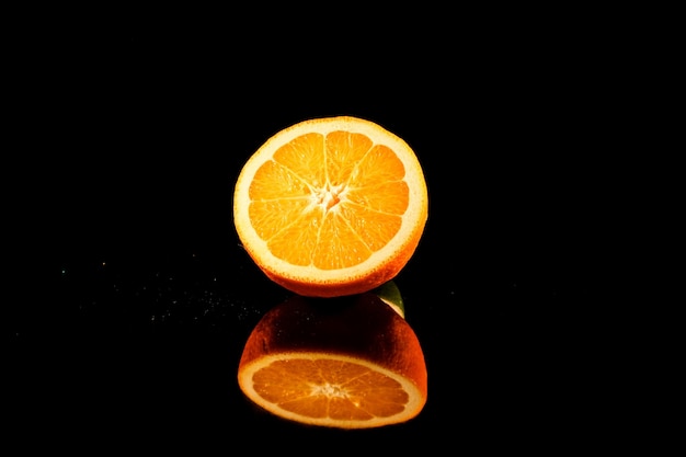 Shiny half of orange stands on black glass table on black background