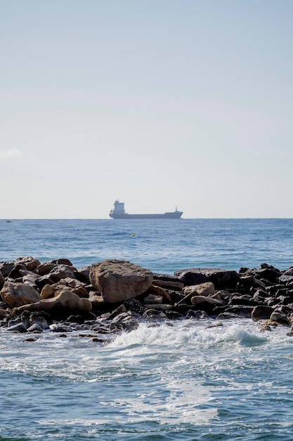 A ship is seen in the distance in front of a rocky outcropping.