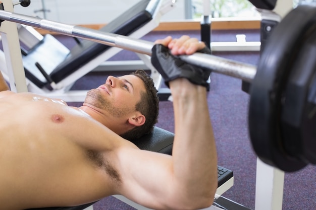 Shirtless bodybuilder lifting heavy barbell weight lying on bench