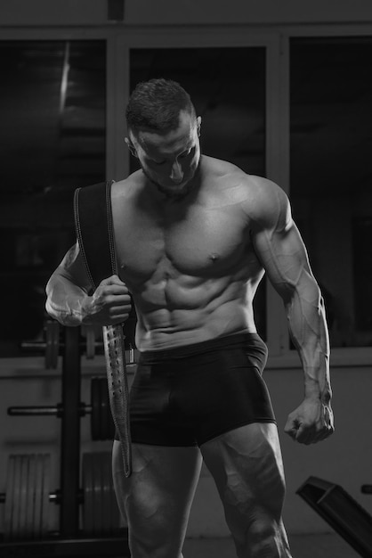 A shirtless bodybuilder with a beard is posing after a workout in a gym