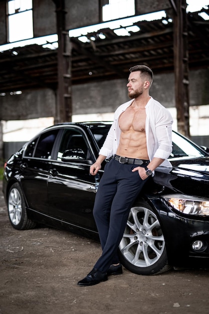 Shirtless bodybuilder with black vehicle Strong muscular man with car standing