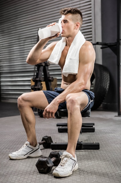 Shirtless man on bench drinking protein shake at the gym