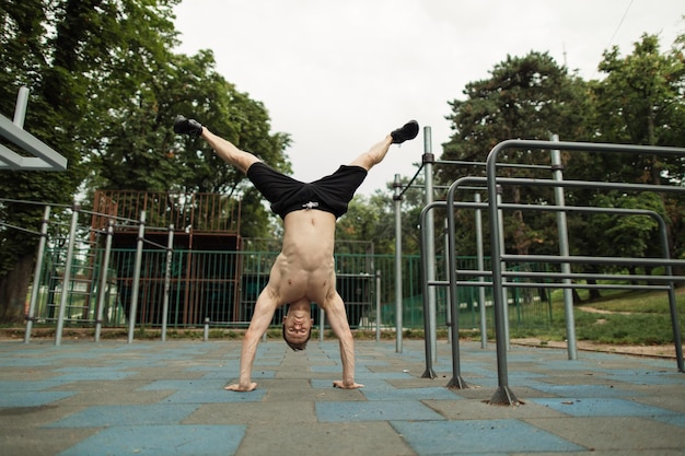 Shirtless man doing a handstand on the outdoor gym