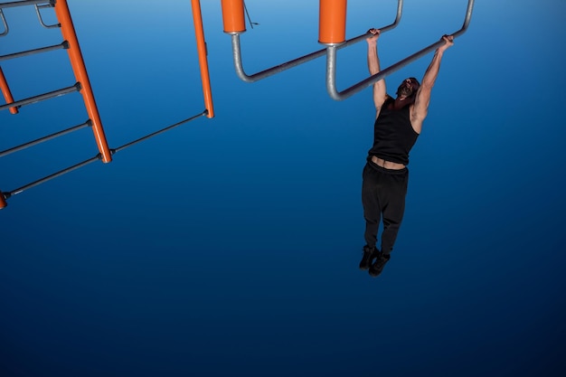 Photo shirtless man doing horizontal balance on parallel bars at sports ground