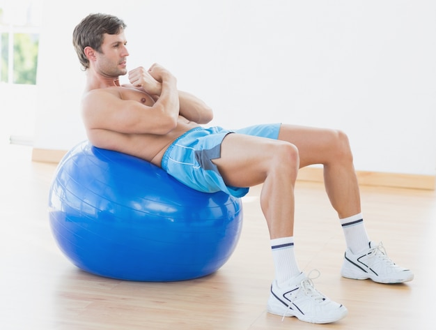 Shirtless man exercising on fitness ball in gym