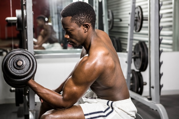 Shirtless man lifting dumbbell on bench at the crossfit gym