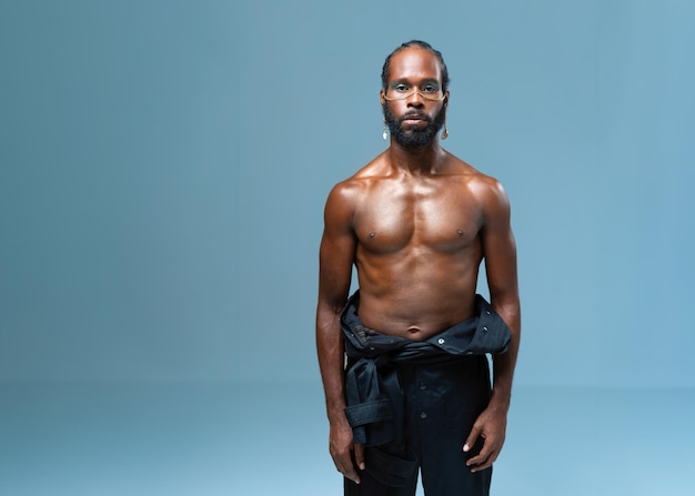 Shirtless muscular black gay man with light makeup in blue studio