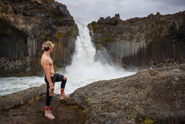 Shirtless and muscular boy looks at the aldeyjarfoss waterfall in iceland