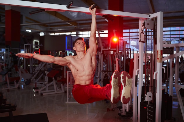 Shirtless sporty male doing ABS workouts on pull up bar in a gym club