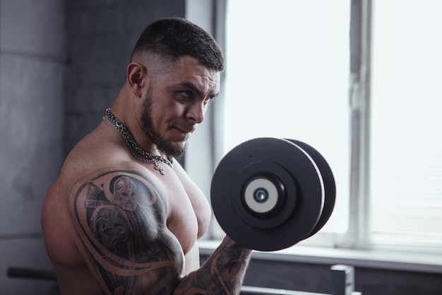 Shirtless tattooed bodybuilder doing dumbbell bicep curls