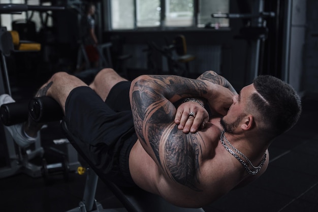 Shirtless tattooed muscular sportsman doing situps at gym