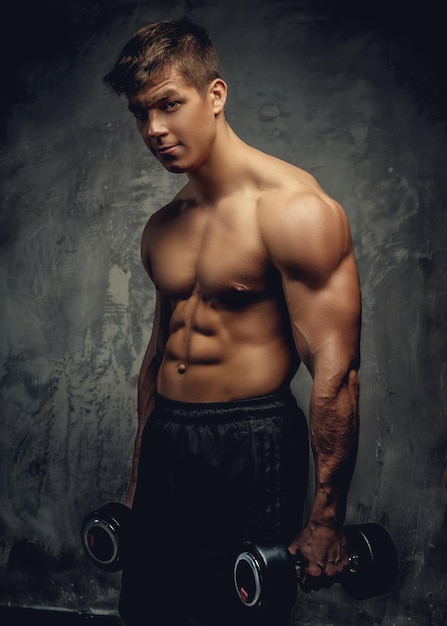 Shirtless young bodybuilder doing exercises with dumbells.