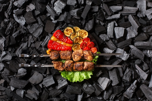 Photo shish kebab on skewers and grilled sweet pepper, zucchini, cherry, tomato on a round plate.