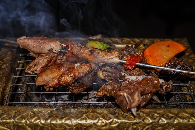 Shish Kebab with vegetables is fried on a golden grill on coals Closeup