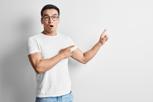 Shocked Asian man dressed in casual and glasses points hands to the side on free space. Surprised young Kazakh man advertises your product on white studio background