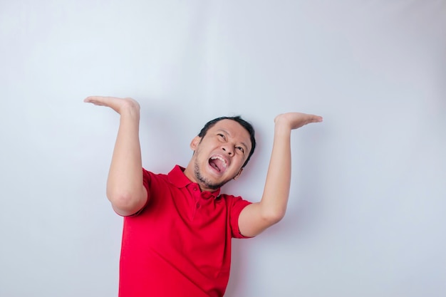 Shocked Asian man wearing a red tshirt pointing at the copy space upside him isolated by a white background