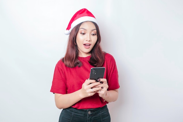 A shocked Asian Santa woman is holding her phone with her mouth wide open isolated by white background Christmas concept