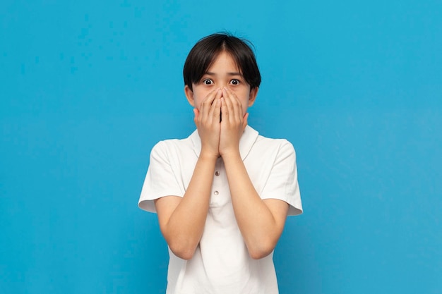 shocked asian teen boy in white tshirt is surprised and covers his mouth with his hands