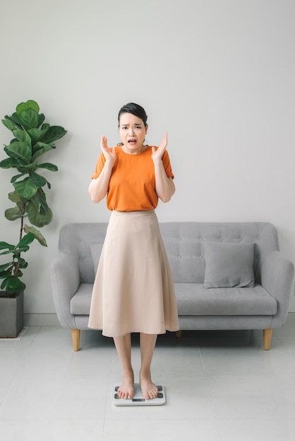 Shocked astonished young woman standing on weighing scale