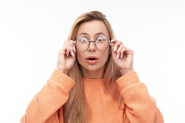 Shocked blond girl face with glasses looks surprised close-up on white studio background with copy space