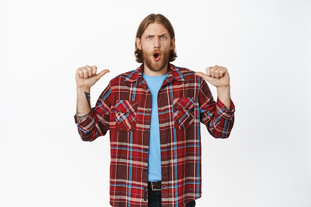 Shocked blond guy pointing at himself with concerned face expression on white.