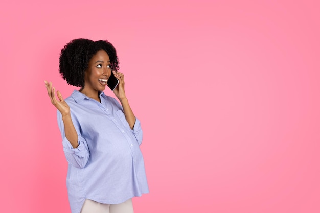 Shocked cheerful millennial black lady with big belly calling by phone speaking