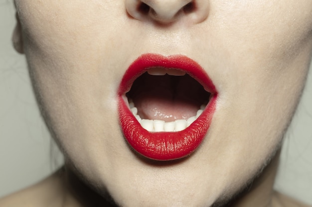 Shocked. Close-up shoot of female mouth with bright red gloss lips make-up and well kept cheeks skin.