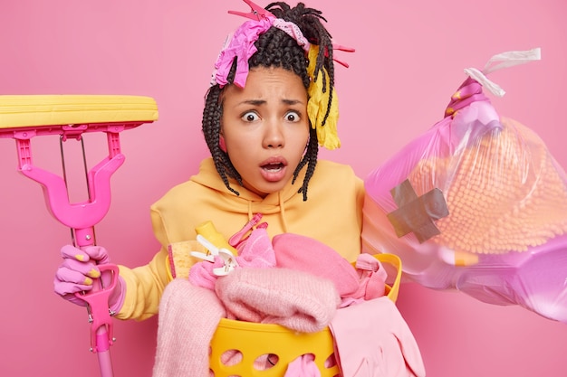 Shocked dark skinned woman with dreadlocks does cleaning at home