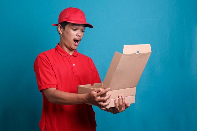 Shocked deliveryman in red uniform open a box of pizza