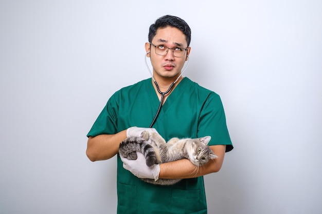 Shocked doctor in vet clinic examining cat with stethoscope gasping amazed while holding cat in his arm